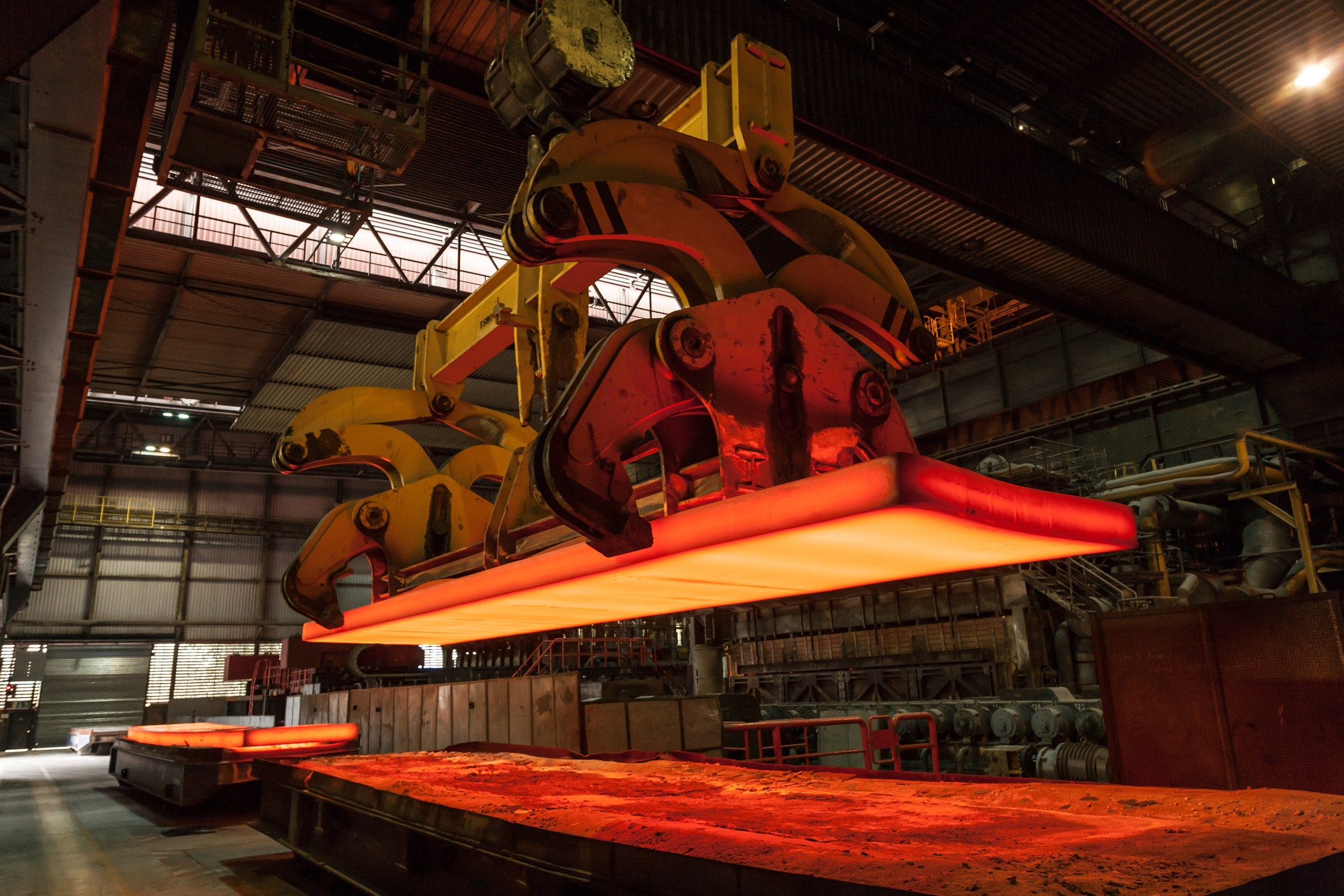 A glowing steel slab is loaded in the steelworks